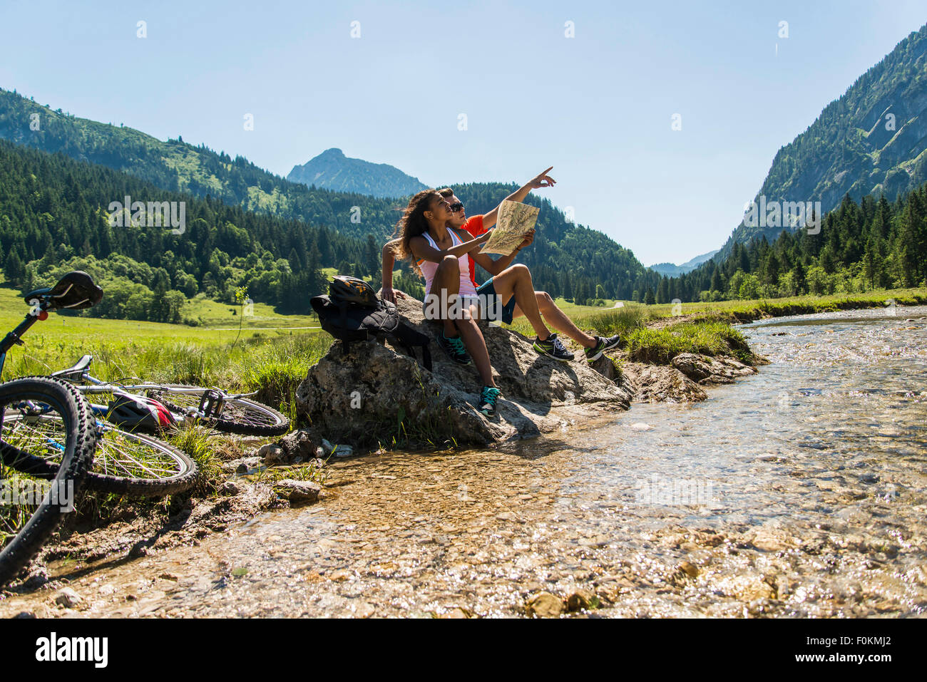 Austria, Tyrol, Tannheim Valley, young couple with mountain bikes and map sitting at brook Stock Photo