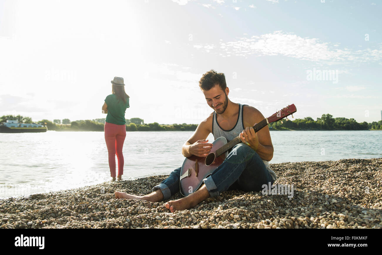 Young man playing guitar with woman by the riverside Stock Photo