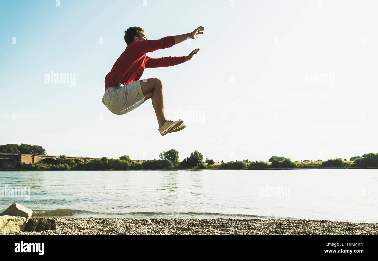 Young man jumping mid-air by the riverside Stock Photo