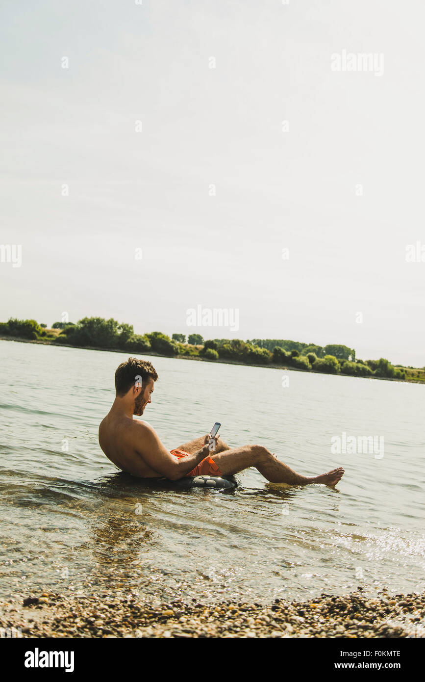 Young man sitting in inner tube in river using smartphone Stock Photo