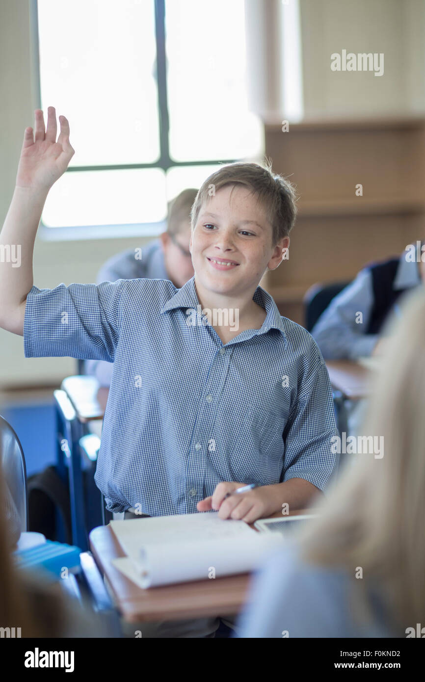 Schoolboy in classroom raising his hand Stock Photo - Alamy