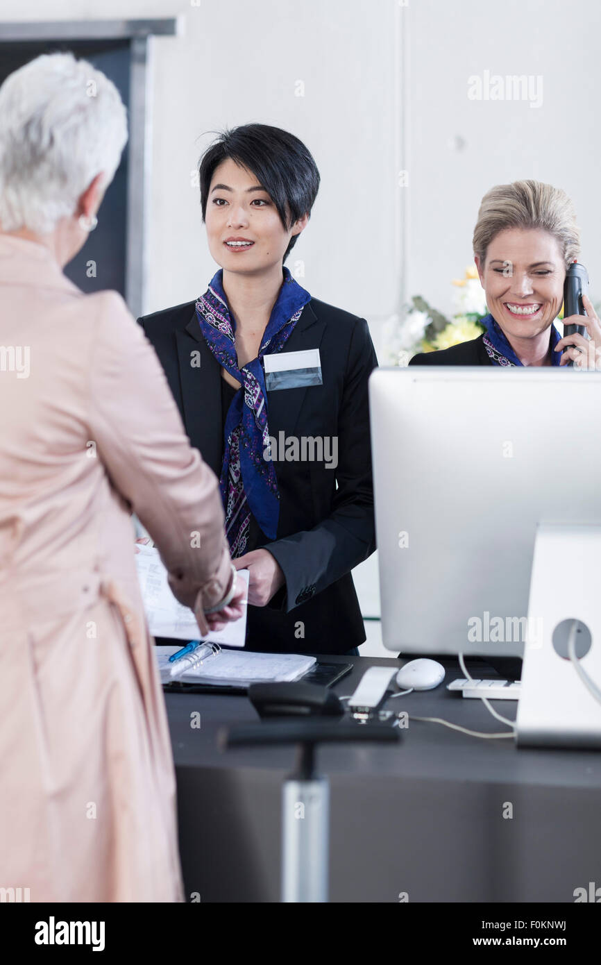 Woman behind reception desk in hotel lobby helping guest Stock Photo