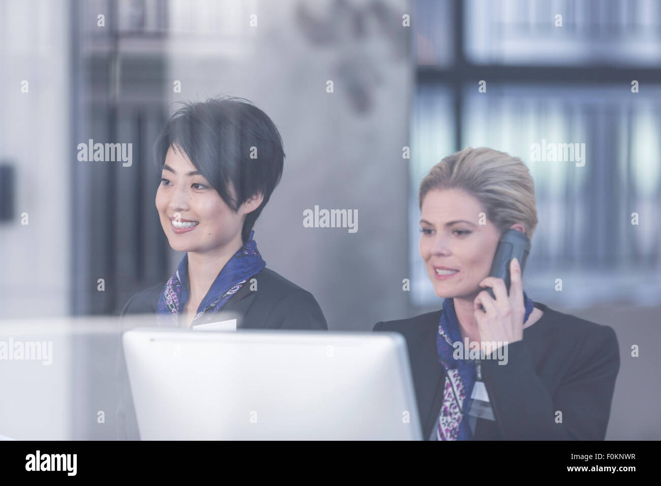 Two women behind reception desk in hotel lobby Stock Photo