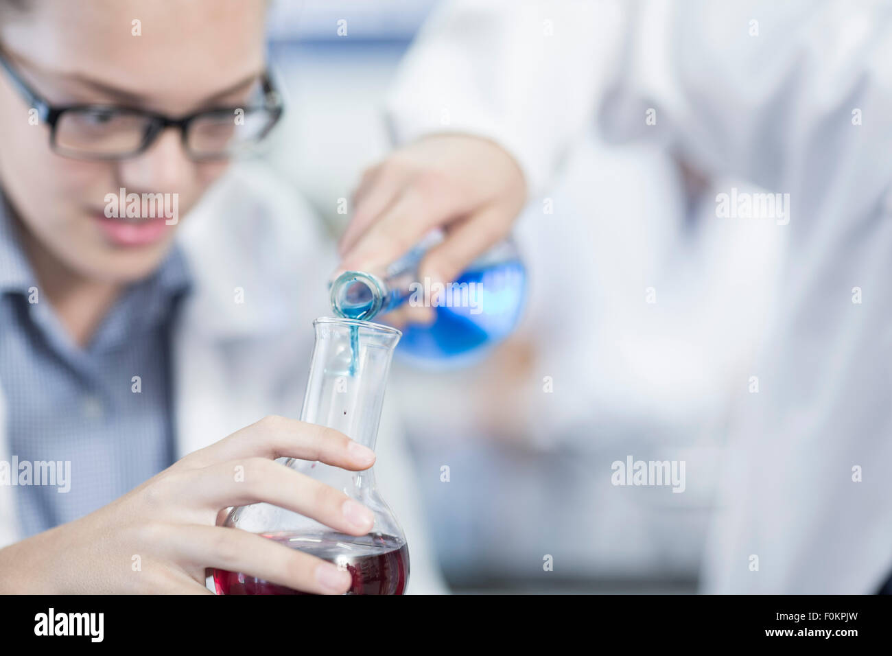 Students in chemistry class pouring liquid into round bottom flask Stock Photo