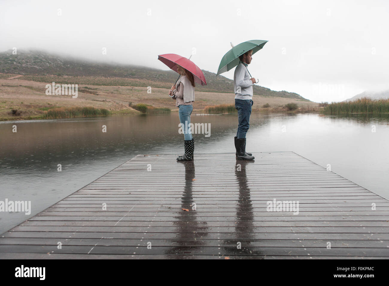 Couple standing in the rain on wooden boardwalk with umbrellas Stock ...