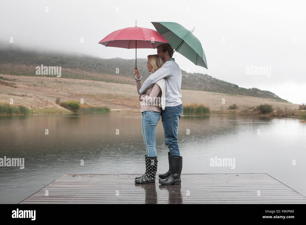 Couple standing in the rain on wooden boardwalk with umbrellas Stock ...