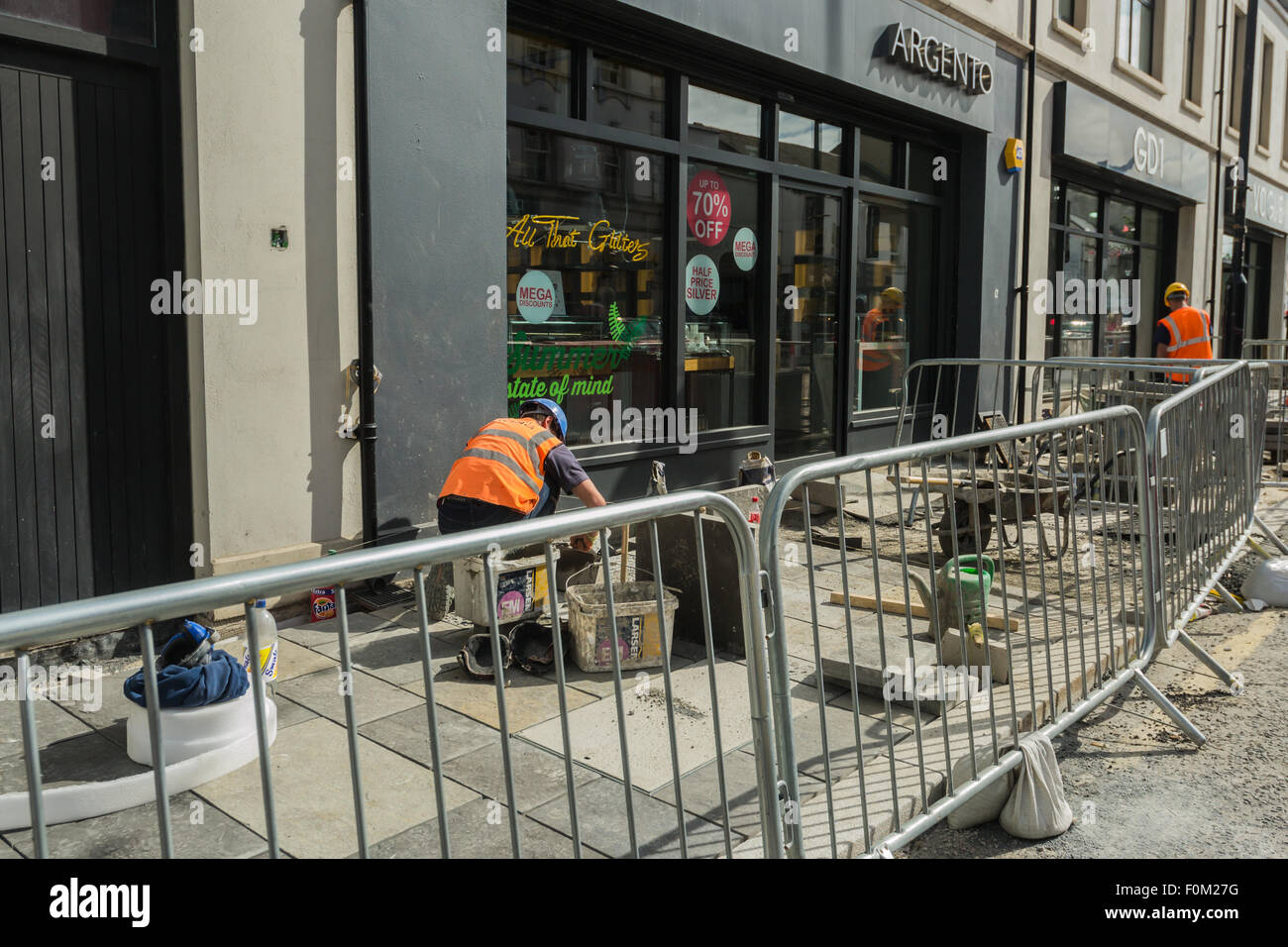 Newtownards, County Down, Northern Ireland, UK.   17th August, 2015.   Public Realm work nearing completion but still disrupting shopping and trade  Members of the public and Public Realm workers  The scheme, which is being match-funded and delivered by the Council, is intended to reinvigorate Newtownards, transforming the visual appearance of the town centre and enhancing its appeal as a place to visit and shop, generating a positive economic impact.  Work is due to be completed for Summer 2016.  Jeffrey Silvers/Alamy Live News Stock Photo