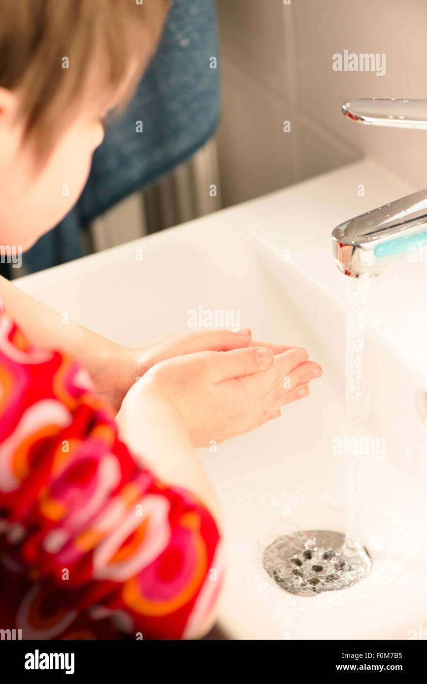 Little girls holding hands over sink with running water. She is washing her hands in a bathroom. Stock Photo