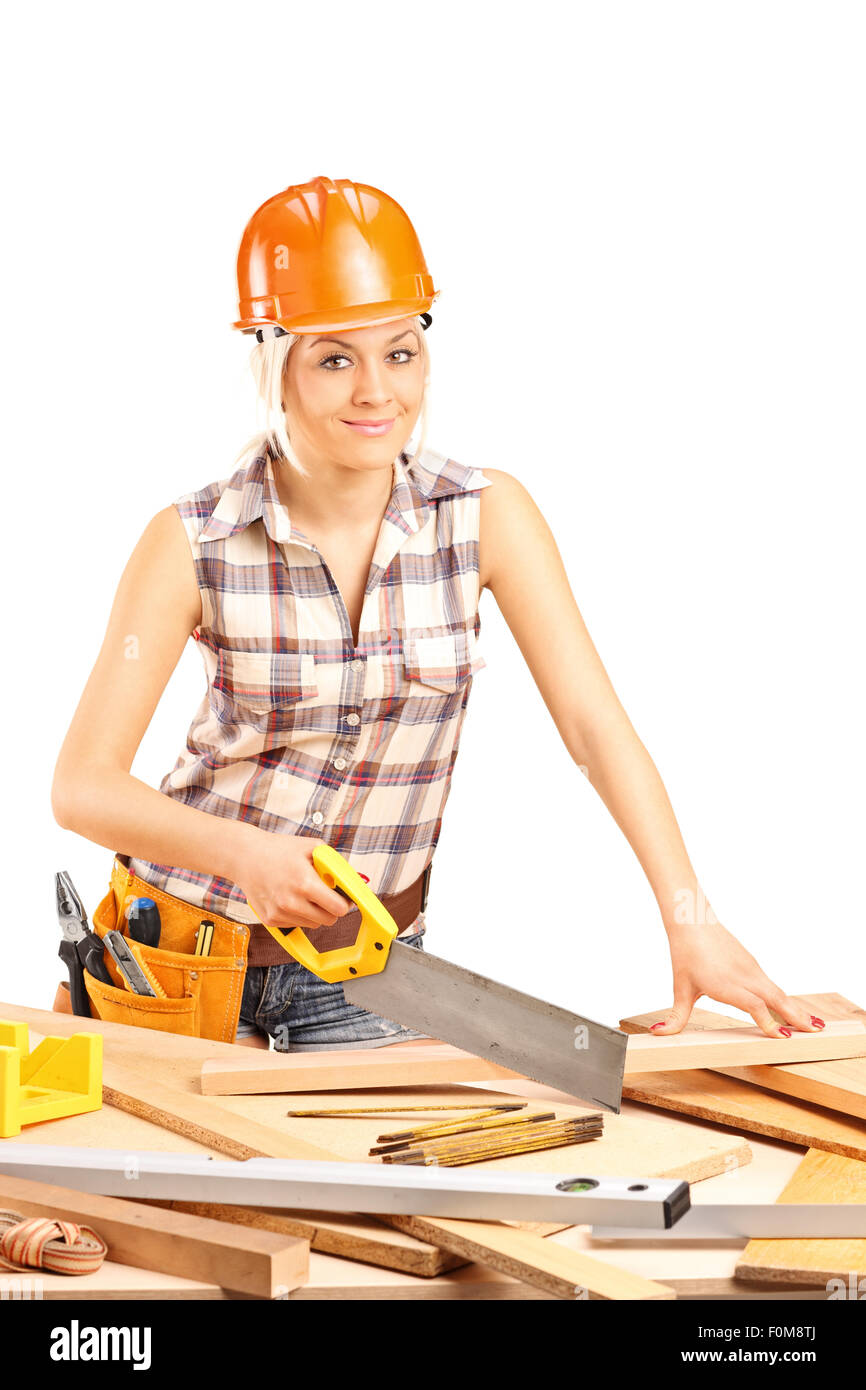 Vertical shot of a female carpenter with an orange helmet cutting a wooden plank with a handsaw isolated on white background Stock Photo