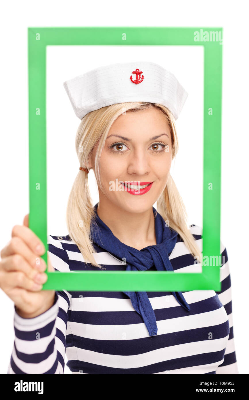 Vertical shot of a young female sailor holding a green picture frame and looking at the camera isolated on white background Stock Photo