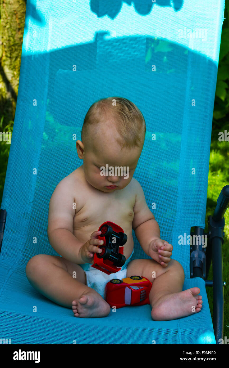 charming caucasian baby boy on chaise lounge in park Stock Photo