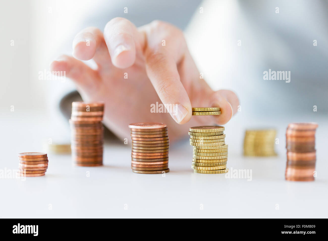 close up of female hand putting coins into columns Stock Photo