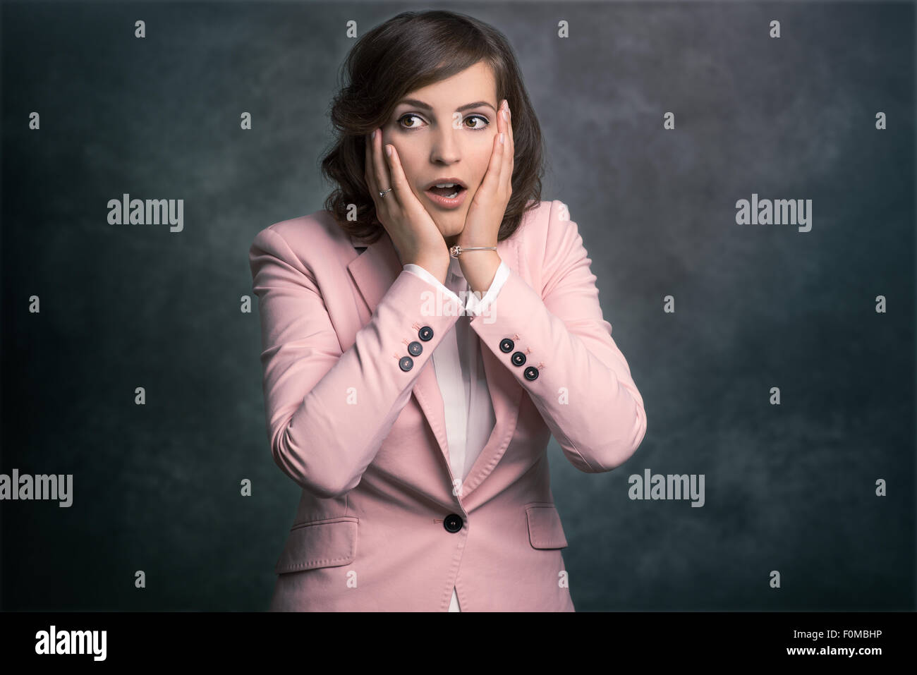 Young woman reacting in shock and horror with her mouth agape and hands raised to her cheeks as she looks sideways to the left o Stock Photo