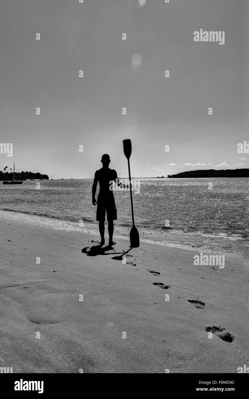 A man carrying an oar silhoutted against the sunlight in Bahia, Brazil Stock Photo