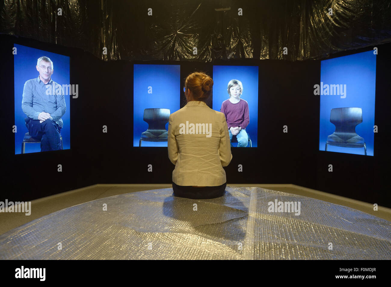 A woman sits in front of a video installation entitled 'Rumpelstilzchen erzaehlen' (Rumpelstiltskins narrating) by Hannah Leonie Prinzler during a pre-opening tour of Grimmwelt (Grimm World) in Kassel, Germany, 18 August 2015. The new exhibition centre on the German folklore collectors and authors Jacob and Wilhelm Grimm is scheduled to open on 04 September 2015. Photo: SWEN PFOERTNER/dpa Stock Photo