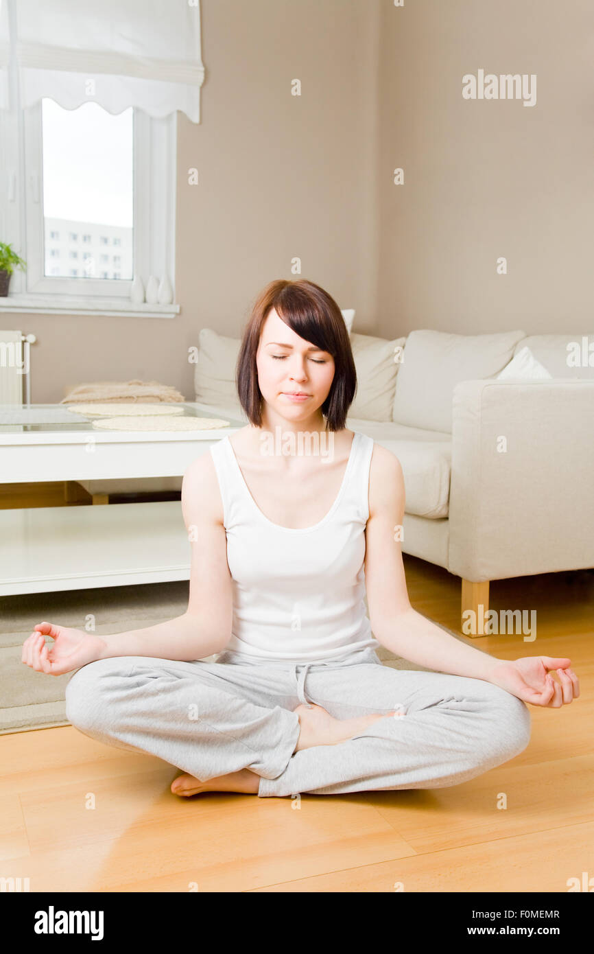 Young woman sitting cross-legged and meditating in her living room Stock Photo