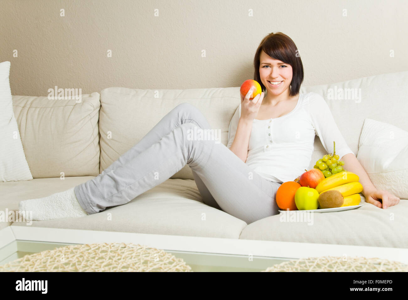 Young woman eating an apple on a couch Stock Photo