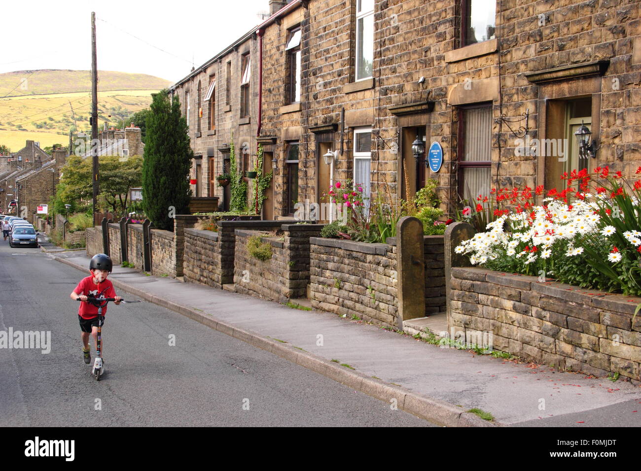 A boy plays on a scooter by terraced houses on Kinder Road in Hayfield village, Peak District, Derbyshire, north England UK Stock Photo