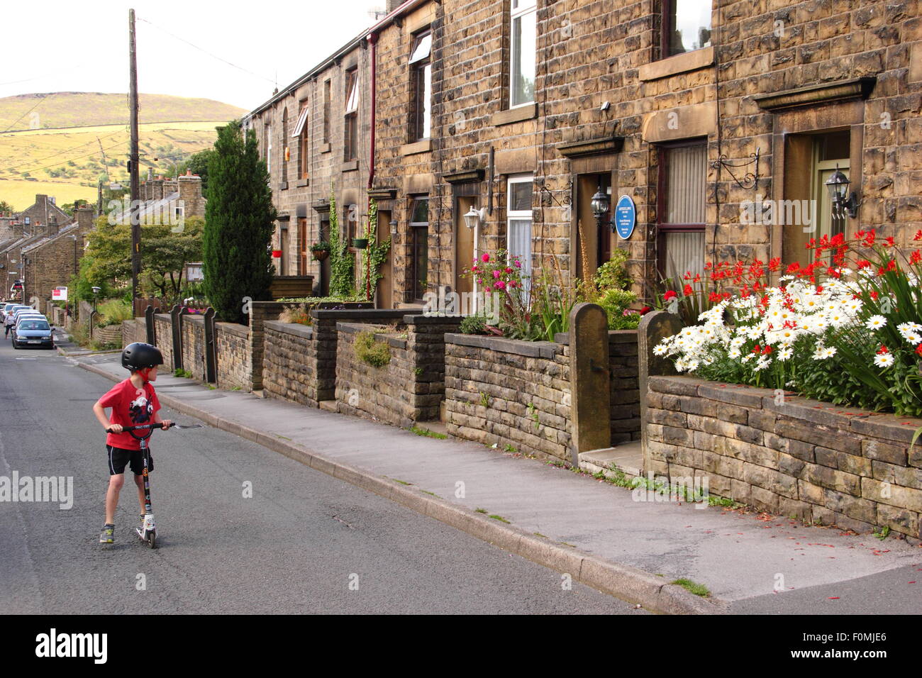A boy plays on a scooter by terraced houses on Kinder Road in Hayfield village, Peak District, Derbyshire, north England UK Stock Photo