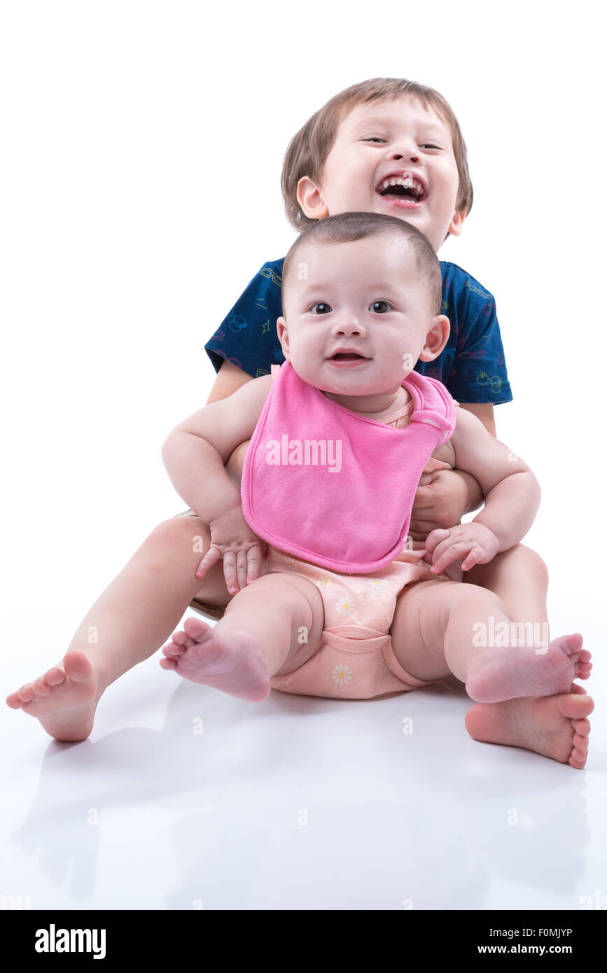 A happy young boy and his baby sister smiling and hugging on a white background. Stock Photo