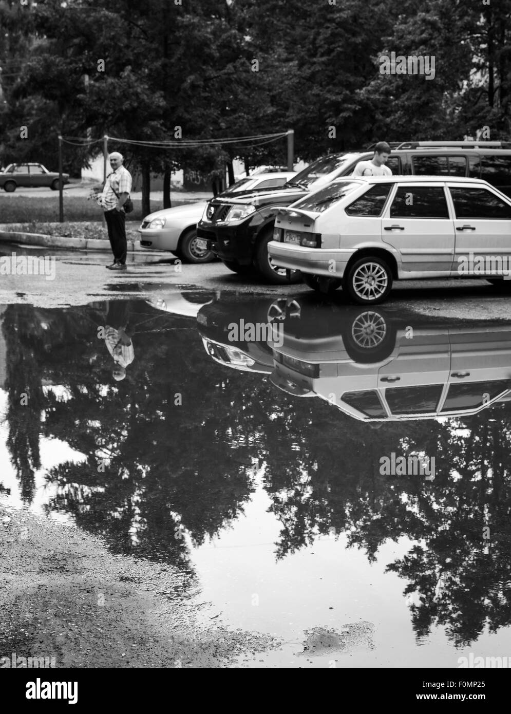 After a heavy rain storm both cars and trees are reflected in a puddle in the road Stock Photo