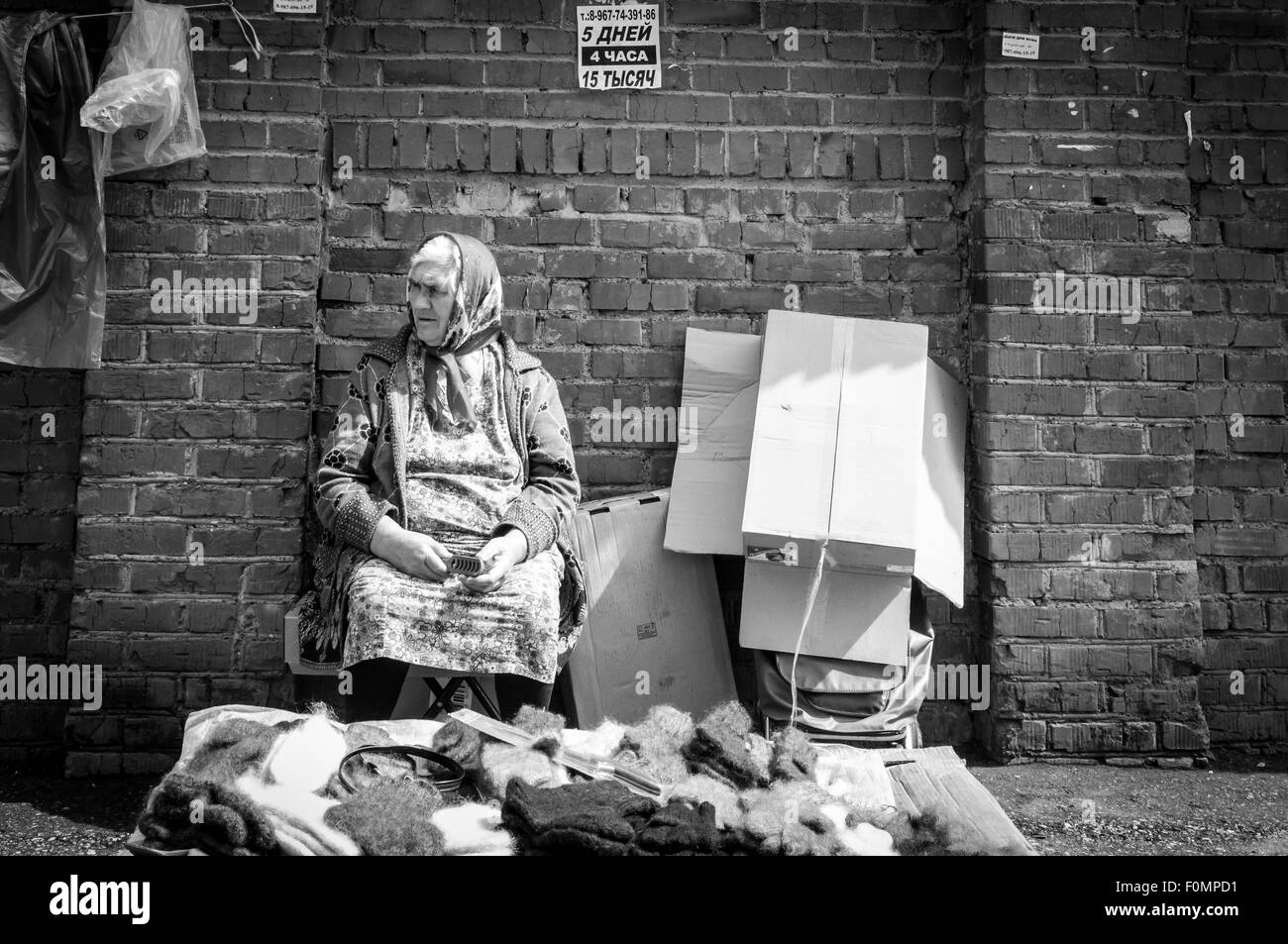 Old pensioner market trader waits for shoppers to purchase woven wool gloves and socks Stock Photo