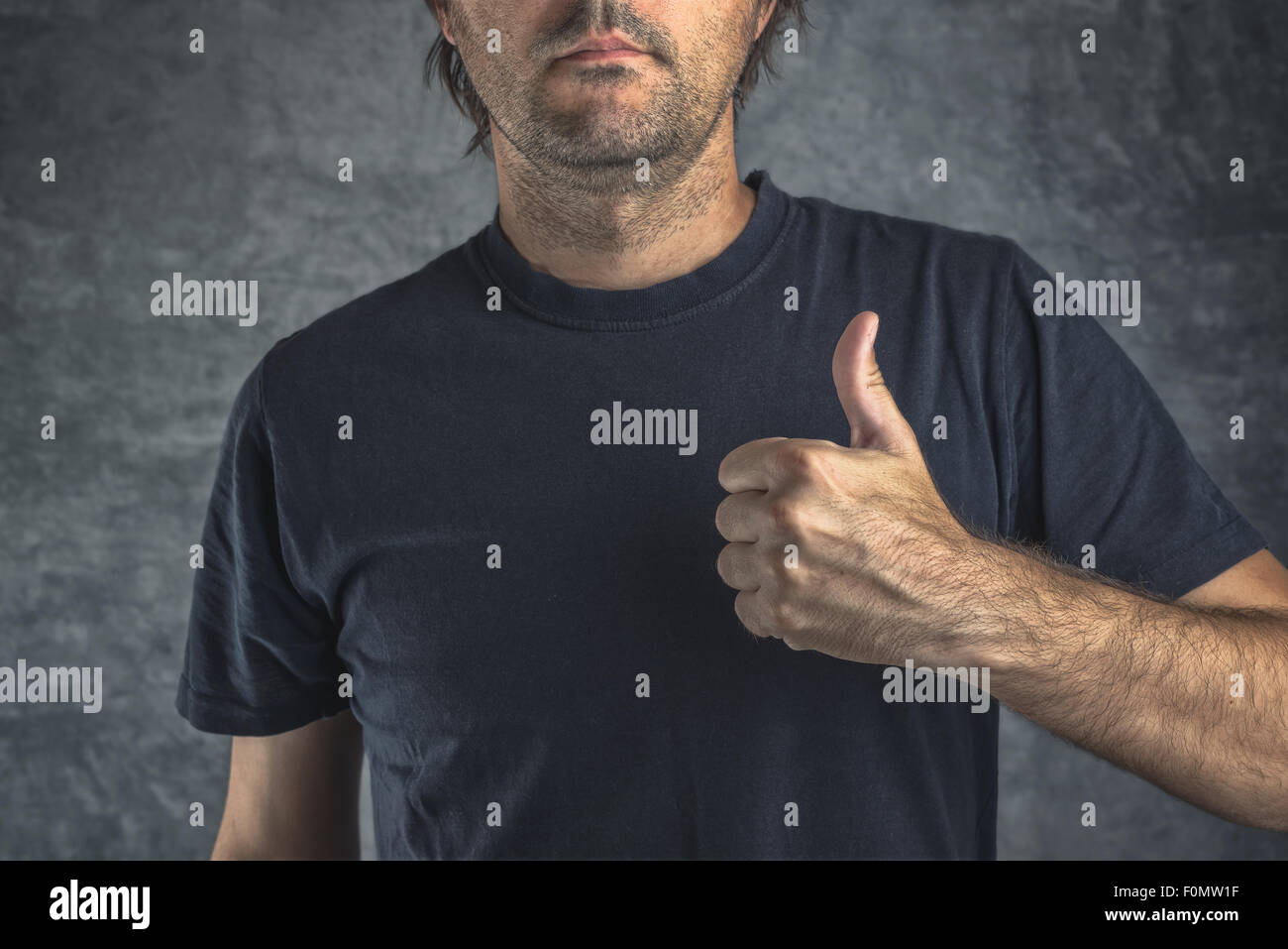 Raised thumb up for approval, adult male in black t-shirt giving endorsement sign Stock Photo