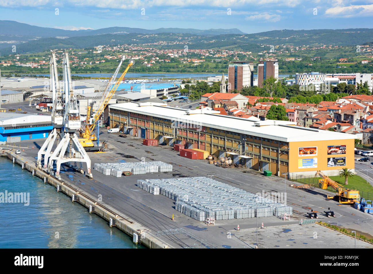 Aerial urban landscape of cranes & large warehouse building stacks of aluminium ingots on dock wharf quayside Port of Koper Slovenia Istrian Peninsula Stock Photo