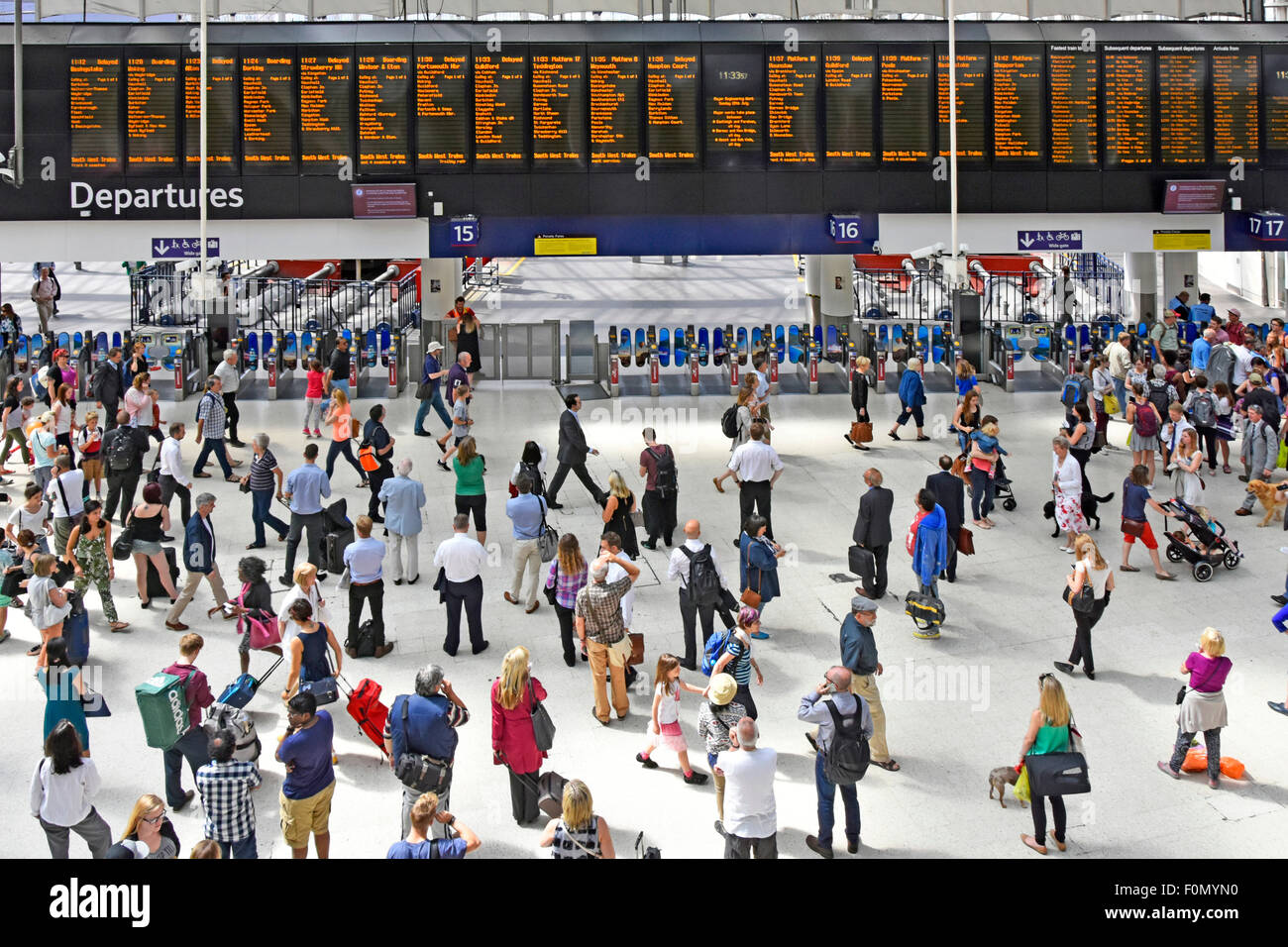 View from above commuters on busy Waterloo train station concourse with departure board and platform entry exit ticket barriers London England UK Stock Photo
