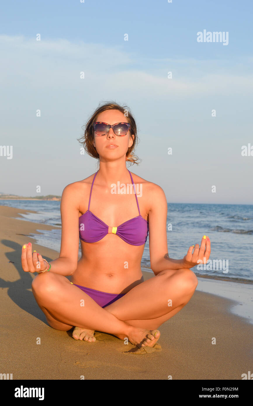 Girl in bikini meditating on the beach facing the sunset Stock Photo
