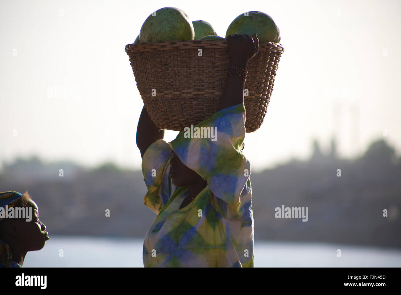 Unidentified Woman carrying vegetables on her head in the streets of Mopti with a young girl Stock Photo