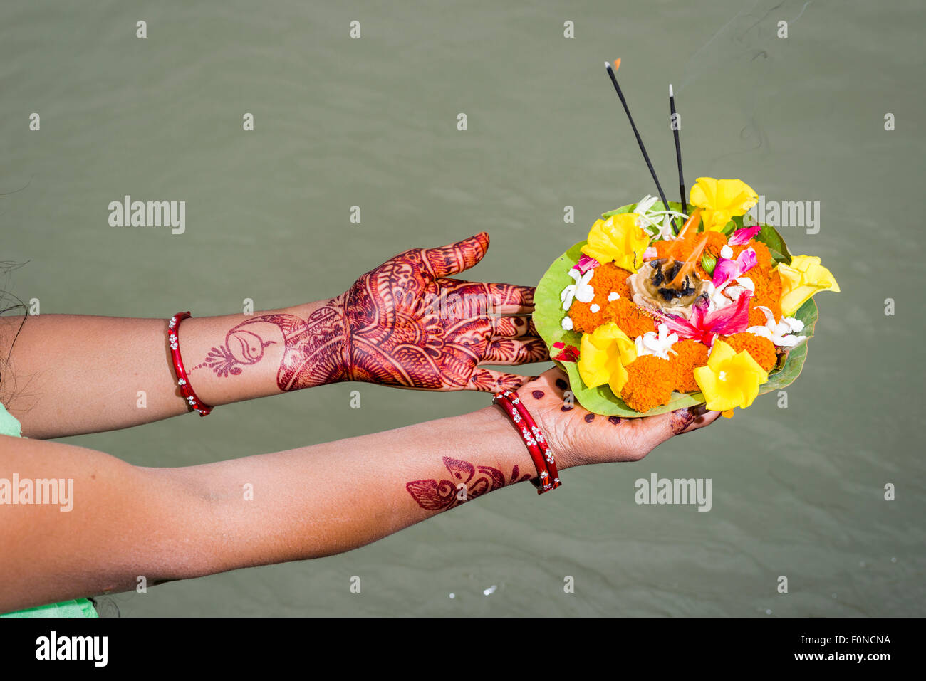 A pair of henna painted hands are holding a deepak, a flower offering, at the ghats of the holy river Ganges, Rishikesh Stock Photo