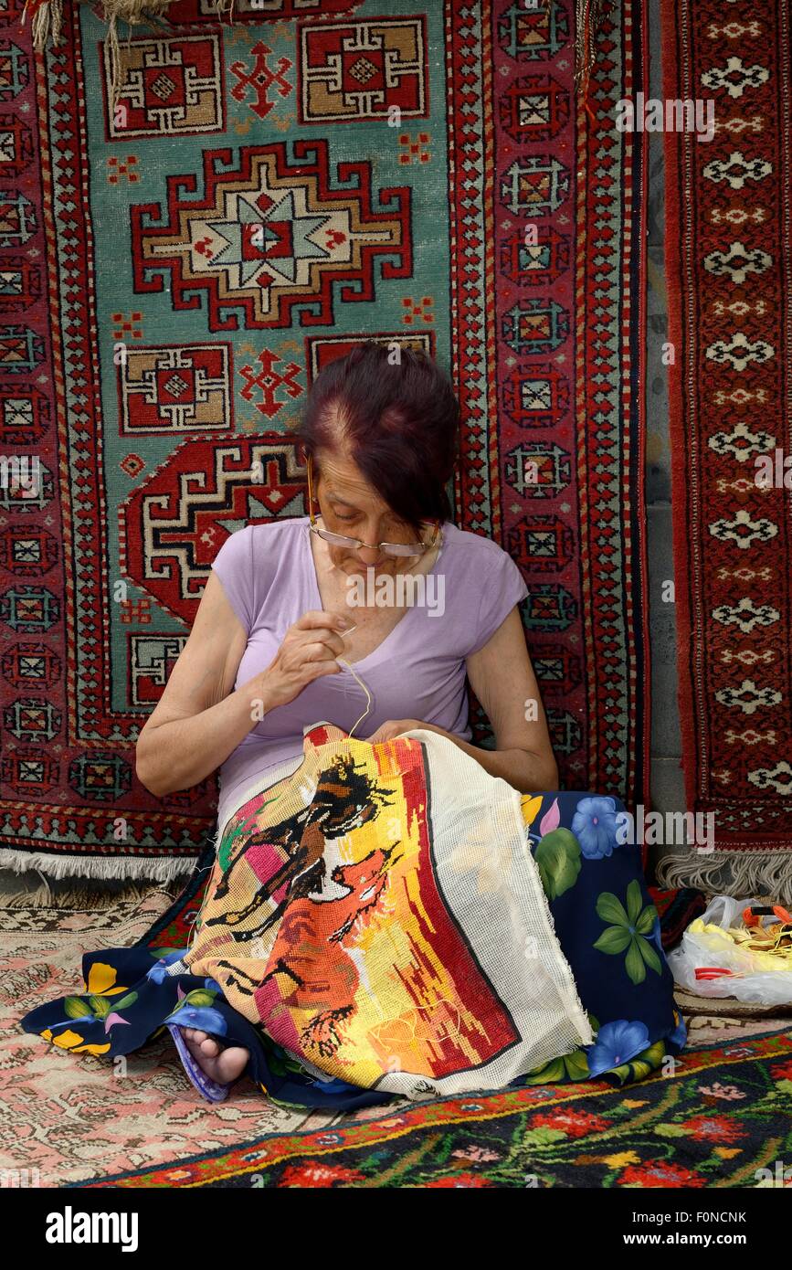 Woman doing embroidery in front of an Armenian carpet, market, Yerevan, Armenia Stock Photo