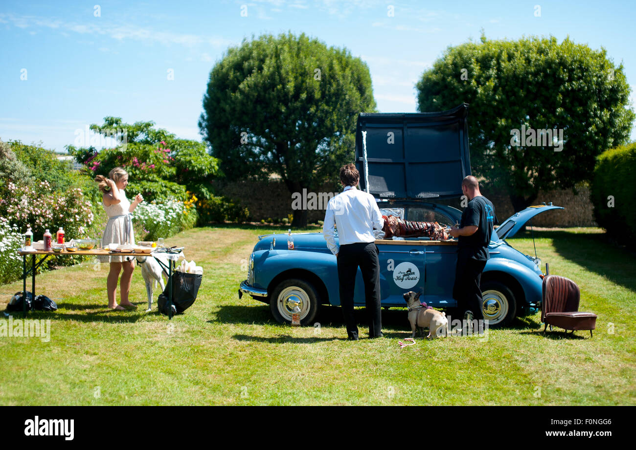 A hog roast being cooked in a 1955 Morris minor split screen at a wedding. Stock Photo
