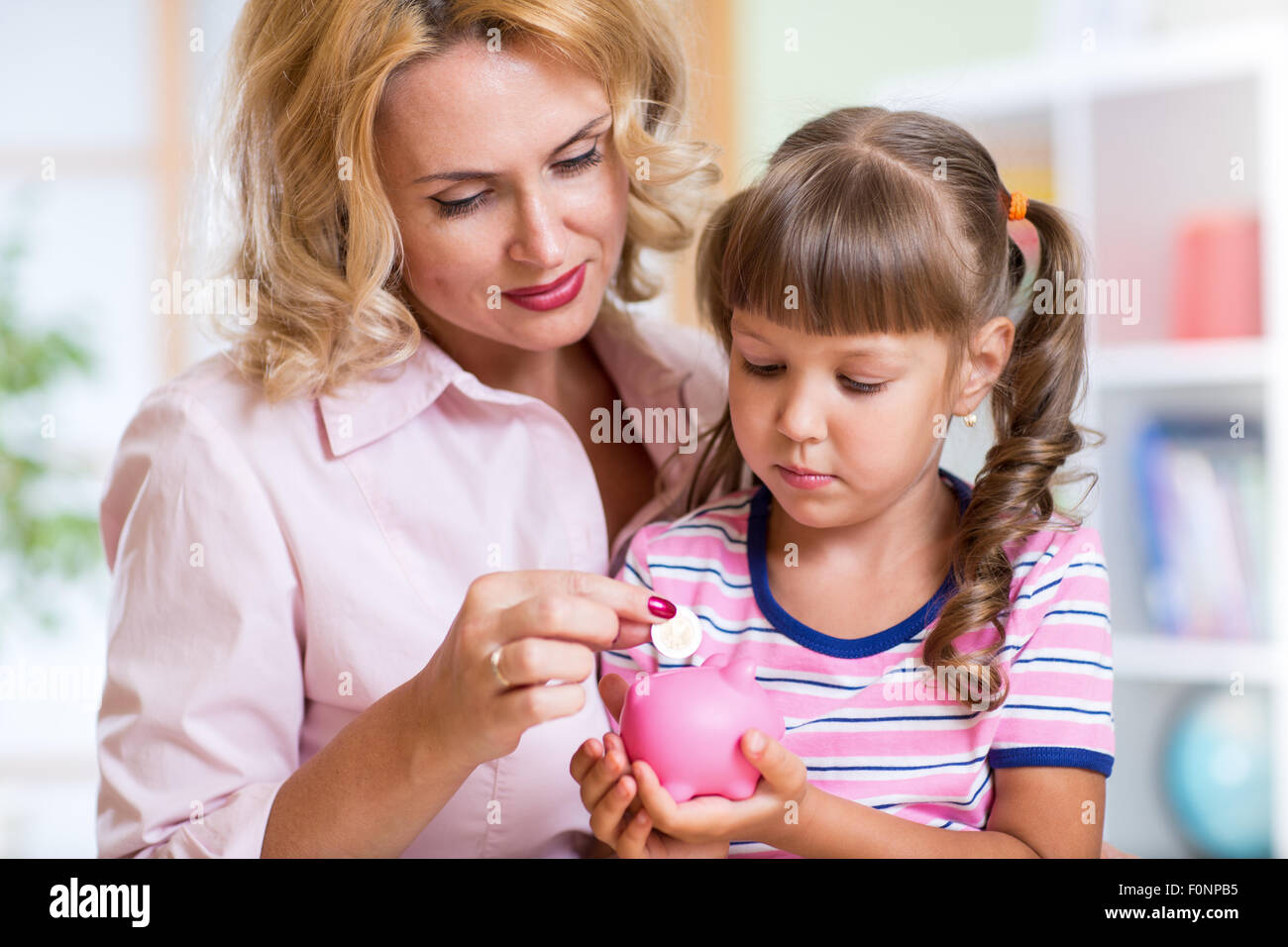 Mother and her daughter putting coins into piggy bank Stock Photo - Alamy