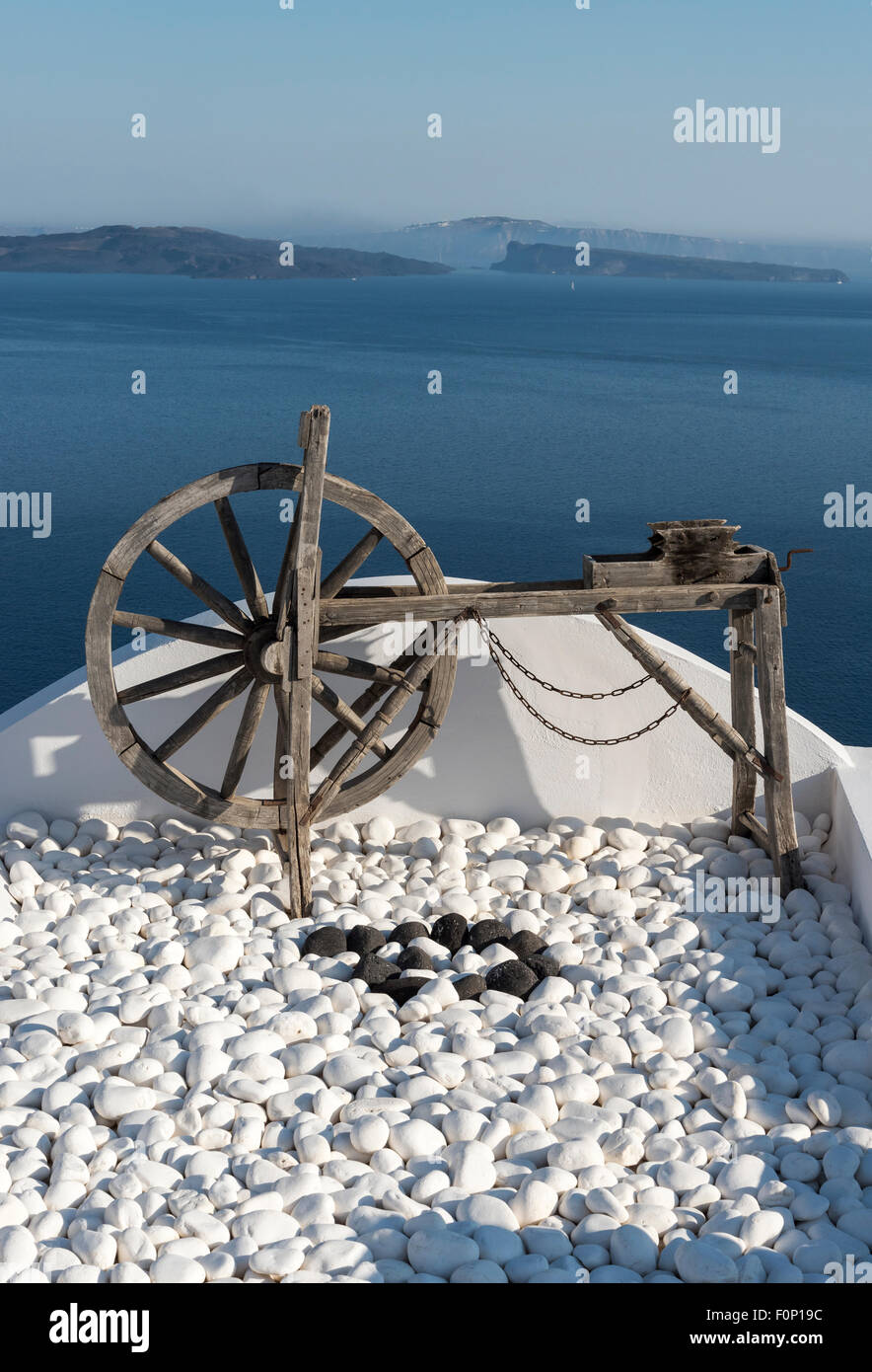 Old Wooden Wheel on White Rooftop Terrace of House in Oia, Santorini, Greece Stock Photo