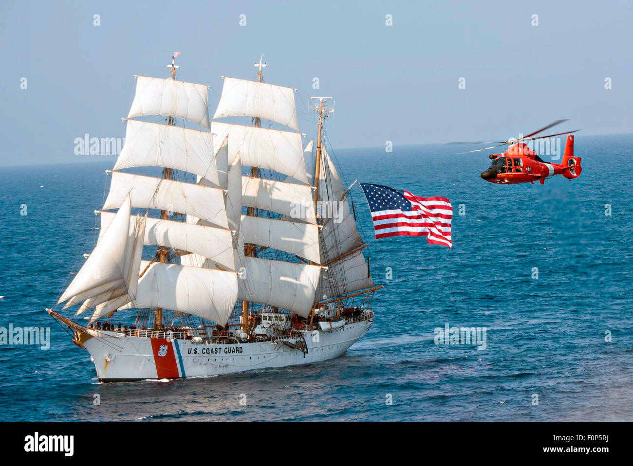 The Coast Guard cutter Eagle sails in the Atlantic Ocean followed by a MH-65 Dolphin helicopter July 30, 2015. The barque Eagle is the only active commissioned sailing vessel in American military service. Stock Photo