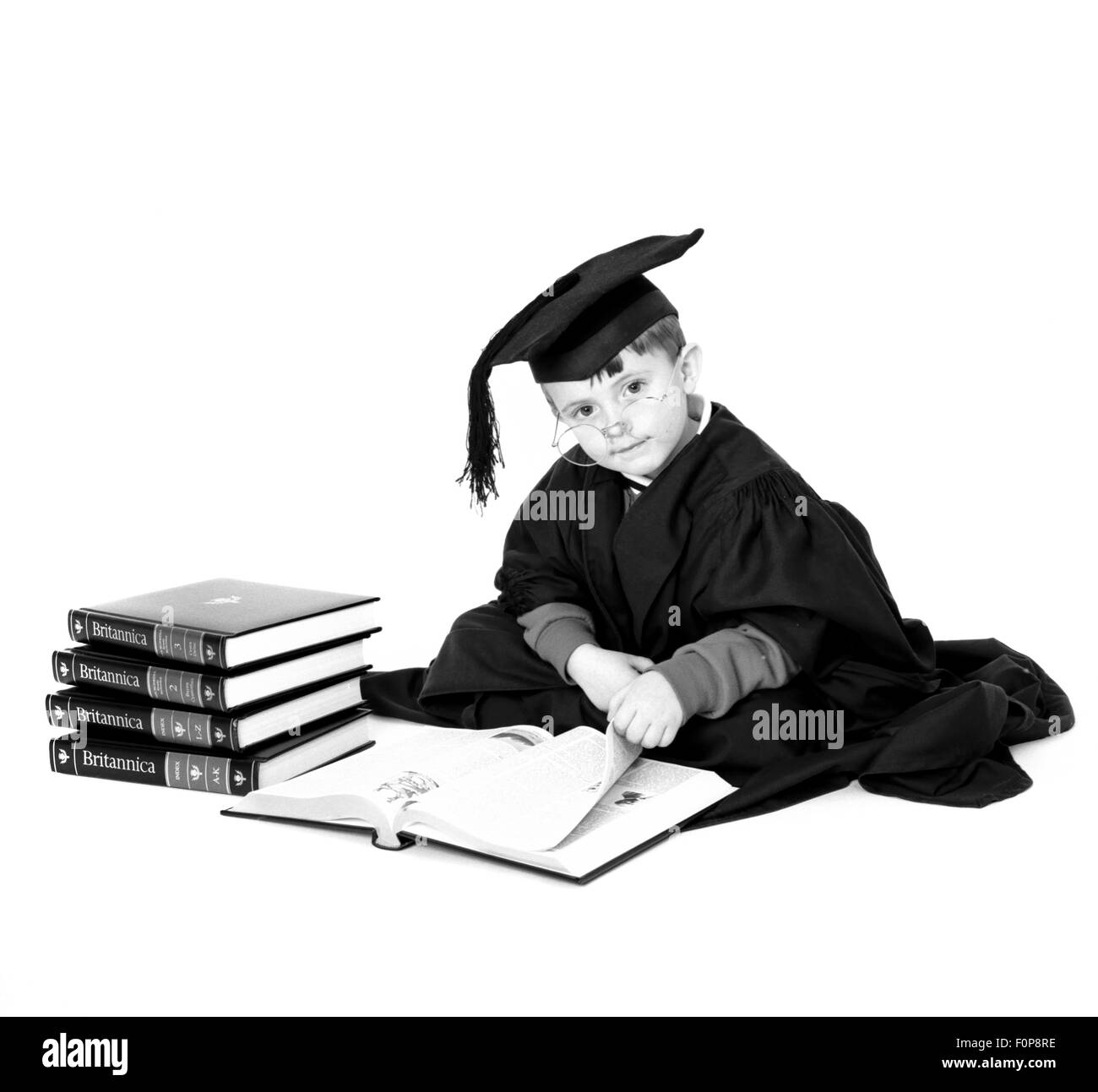 Young boy dressed in mortar board and gown reading Encyclopaedia Britannica Stock Photo