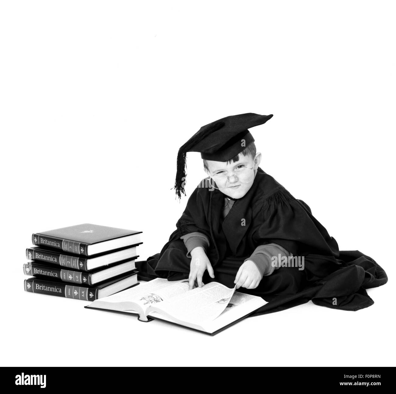 Young boy dressed in mortar board and gown reading Encyclopaedia Britannica Stock Photo