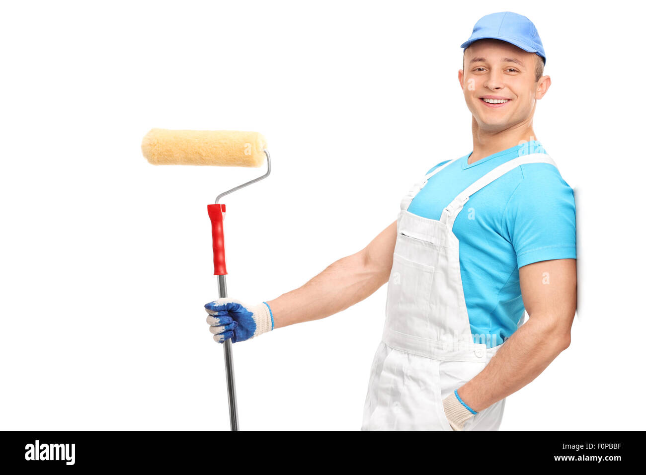 Relaxed young painter in a white jumpsuit holding a paint roller and leaning against a wall