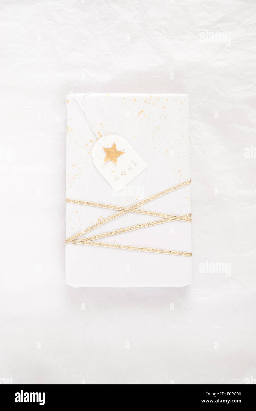 simple gift wrapping with white tissue paper splattered with random gold paint and decorated with gold ribbon and tag Stock Photo