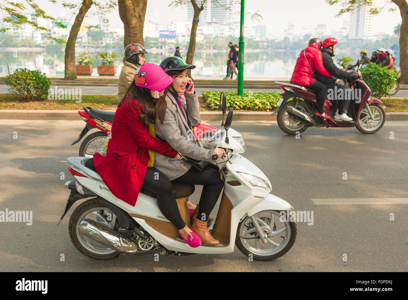 Female friends friendship, view of two young women riding a motorbike together on West Lake Causeway in Hanoi, Vietnam Stock Photo