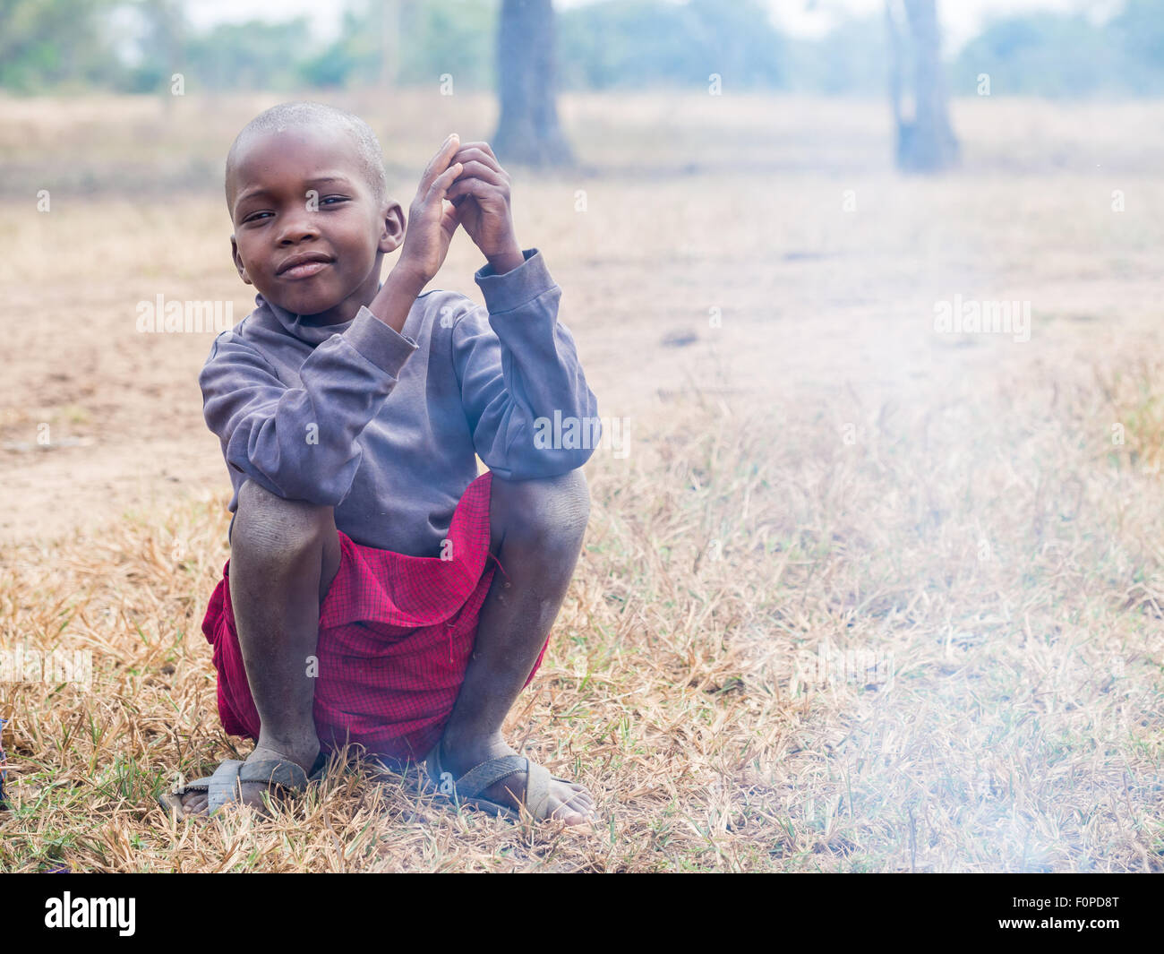 Maasai child sitting next to a fire in his boma (village) in Tanzania, Africa. Stock Photo