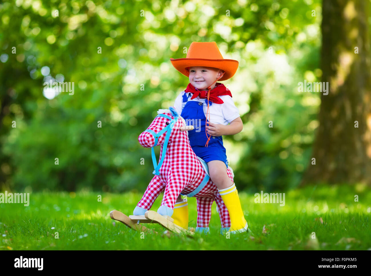 Little boy dressed up as cowboy playing with his toy rocking horse in a