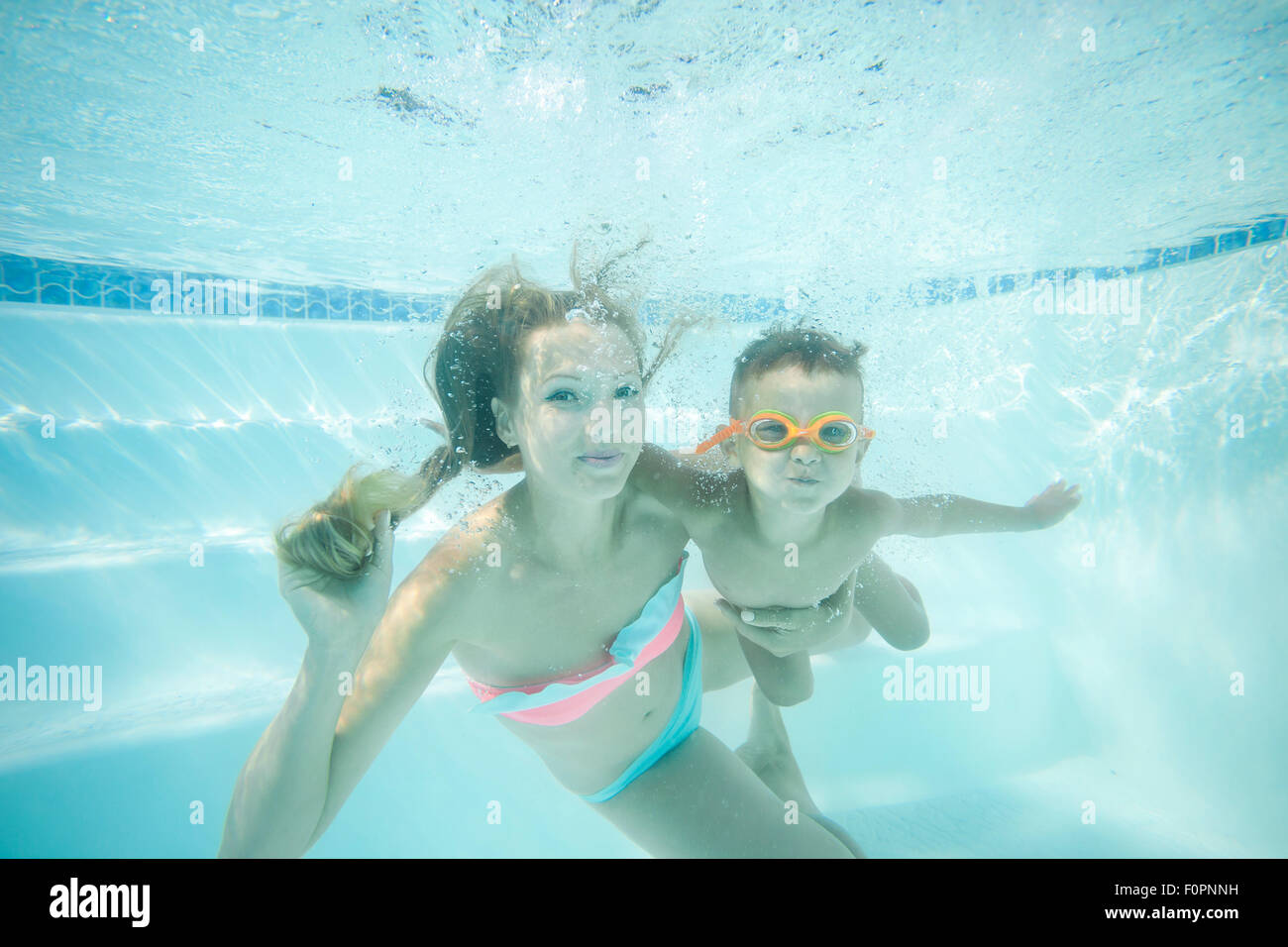 Young mother and toddler son swimming underwater in pool and having fun