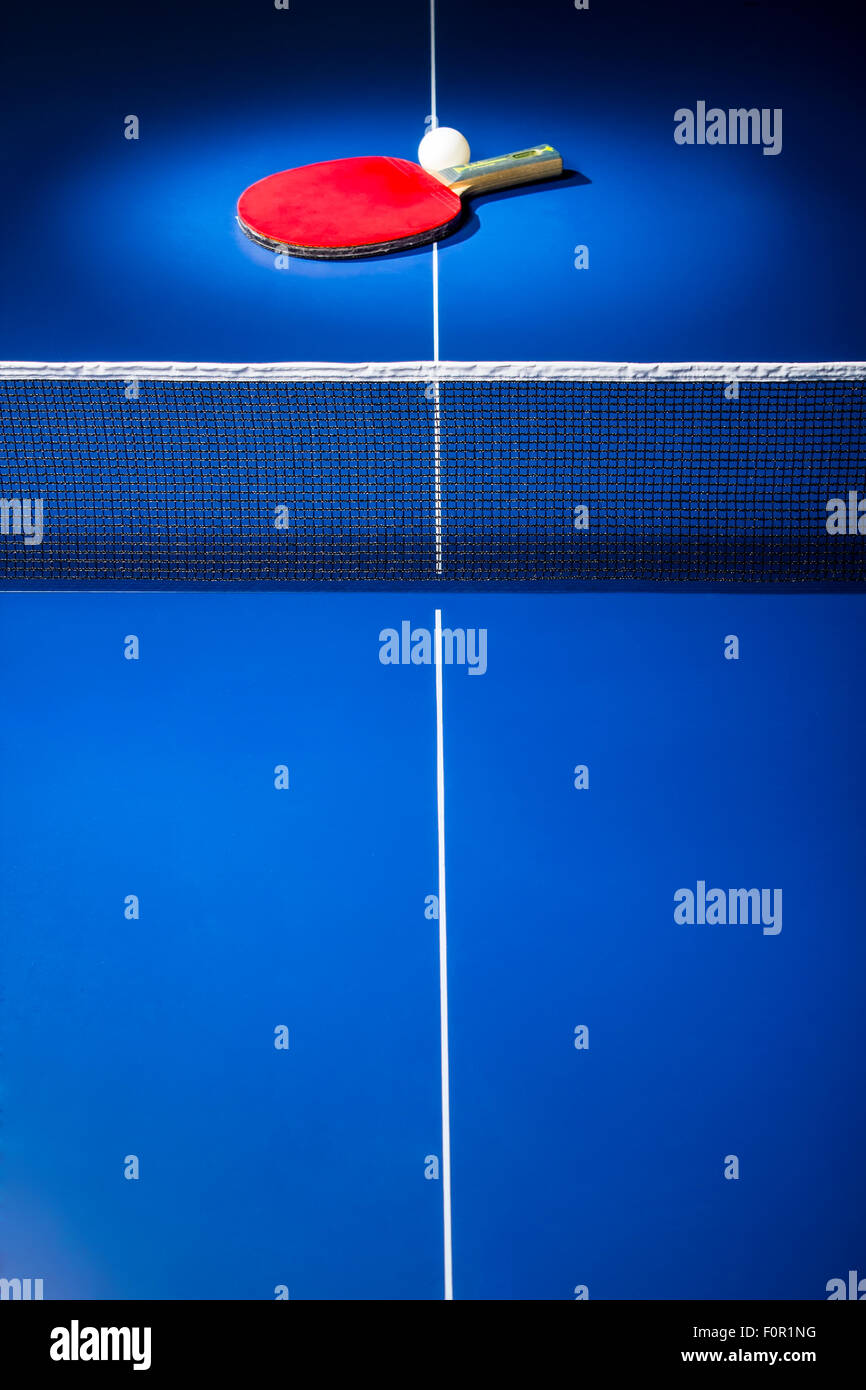 Table tennis paddle and ball displayed in the spotlight on blue ping pong table. Stock Photo