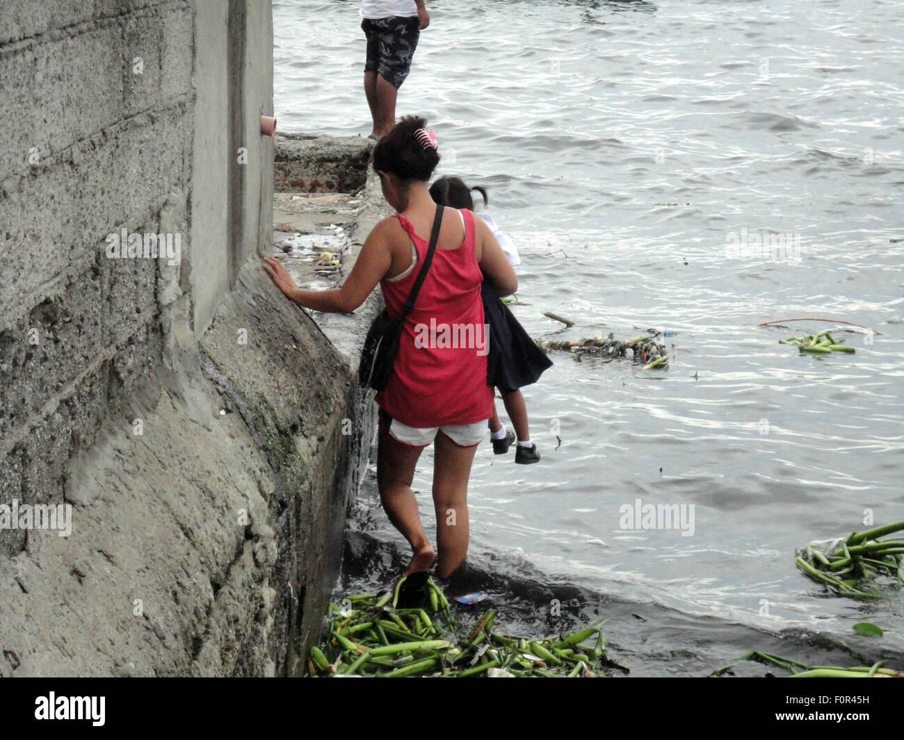 Navotas City, Philippines. 20th Aug, 2015. A Filipino woman carries her child along the coast of Manila Bay in Navotas City, north of Manila, Philippines. Typhoon Goni has slowed down after entering the Philippine Area of Responsibility (PAR) on Tuesday, and is expected to become a super typhoon over the weekend as it travels through the northern Luzon island in the Philippines, slightly hitting Taiwan, then heading north towards Japan and South Korea. Credit:  Richard James Mendoza/Pacific Press/Alamy Live News Stock Photo