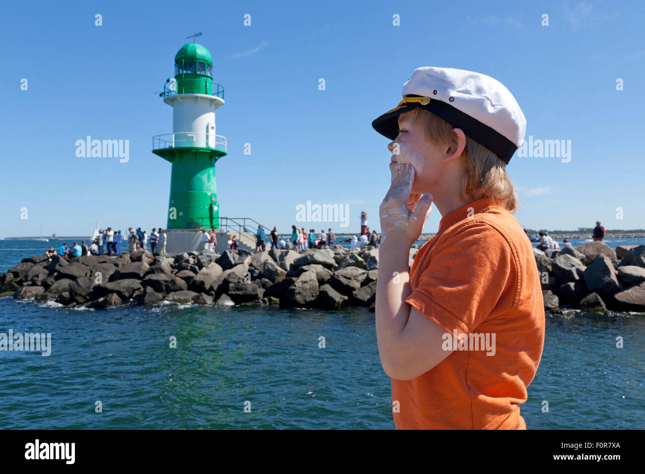 young captain applying sunscreen to his face in front of lighthouse, Warnemuende, Rostock, Mecklenburg-West Pomerania, Germany Stock Photo
