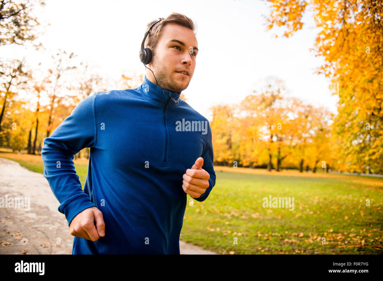 Young man with headphones running in autumn nature and listening music Stock Photo