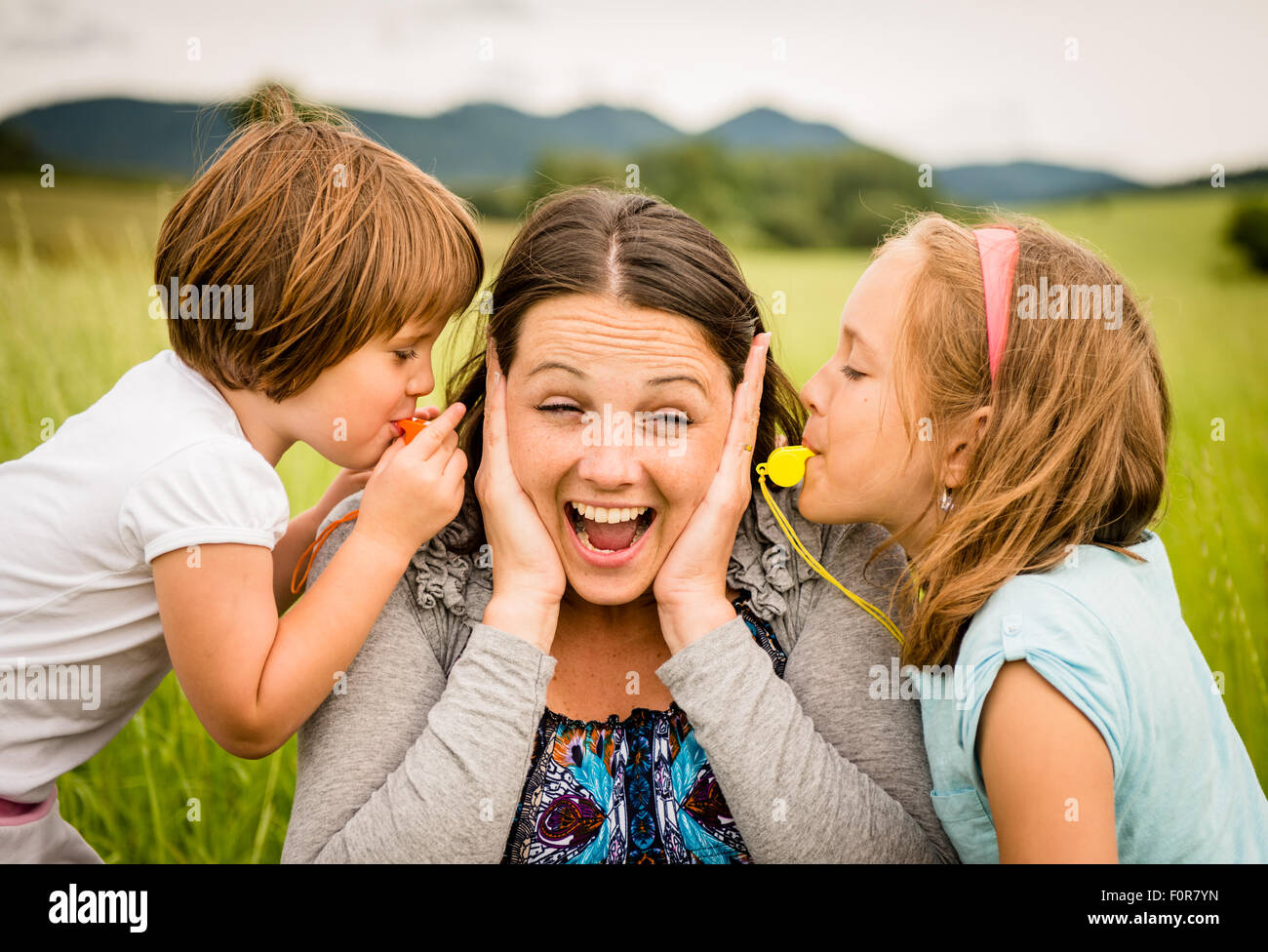 Children blowing whistles to mother's ears- outdoor in nature Stock Photo